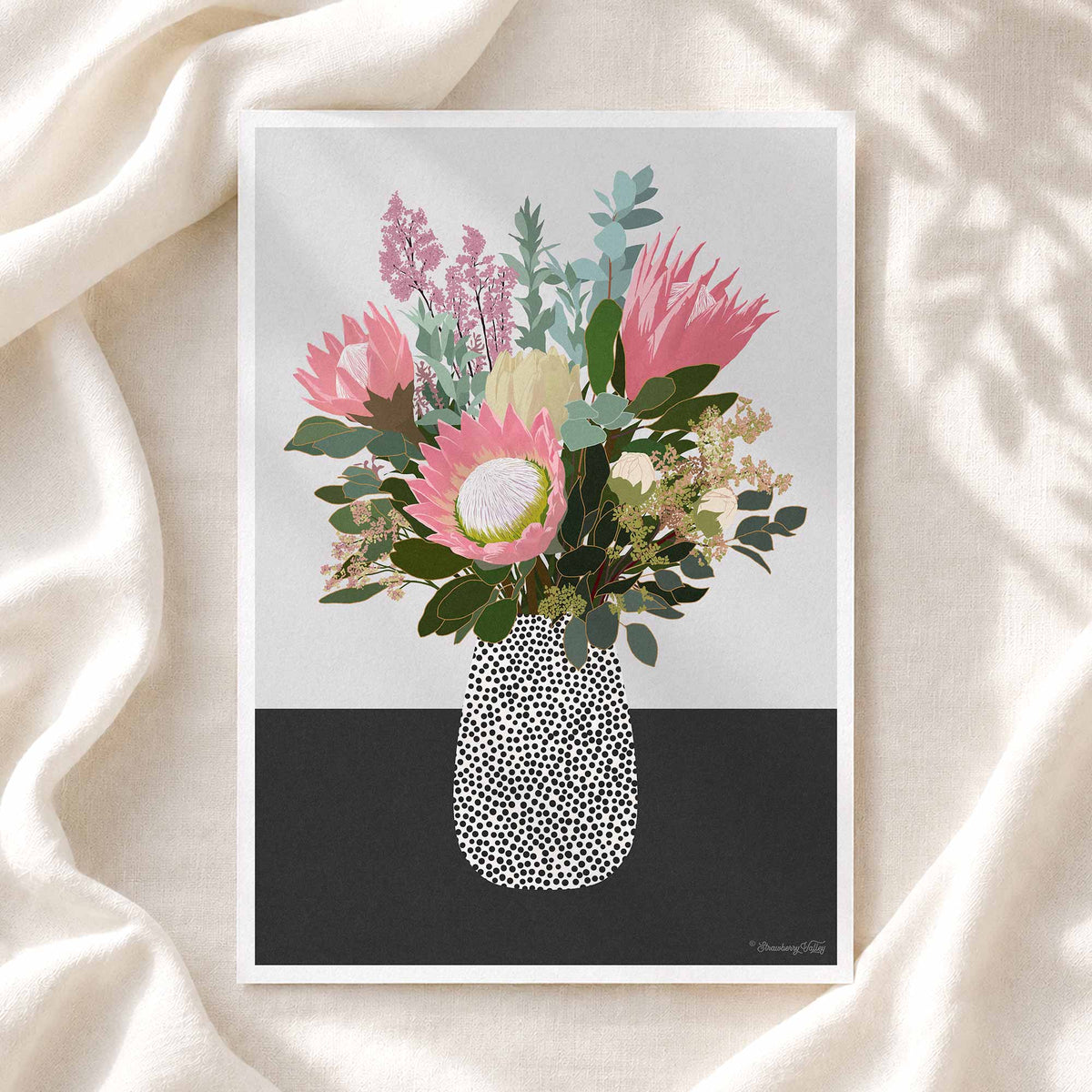A framed floral art print featuring a bouquet of pink protea flowers, green foliage, and cream blossoms in a black-and-white speckled vase, displayed on draped cream fabric with soft shadow overlays.