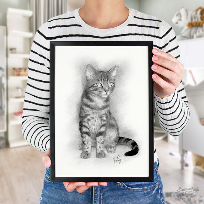 woman ina  black and white striped top holding a pet portrait of a cat