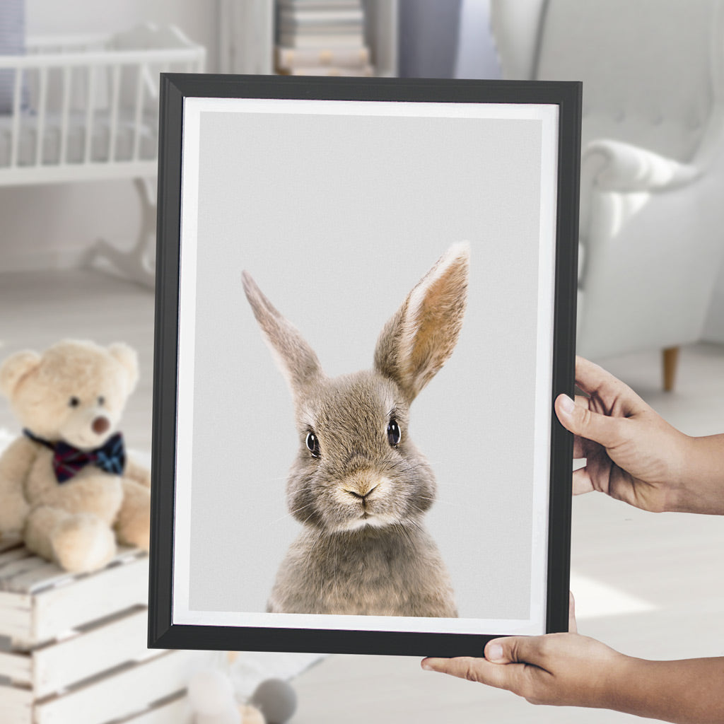 a picture of a brown rabbit in a black frame, being held by a woman standing in a child's nursery