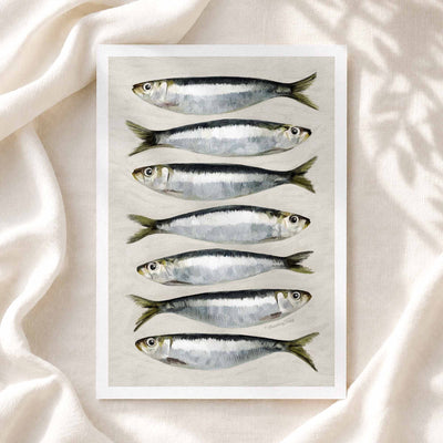 A framed art print featuring a vertical illustration of seven silver and black fish on a light background, styled on draped cream-colored fabric.